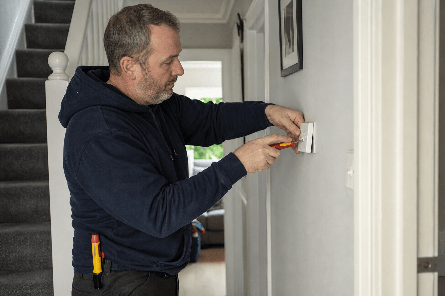 UK homeowner removing a light switch faceplate with a GS38 tester on belt