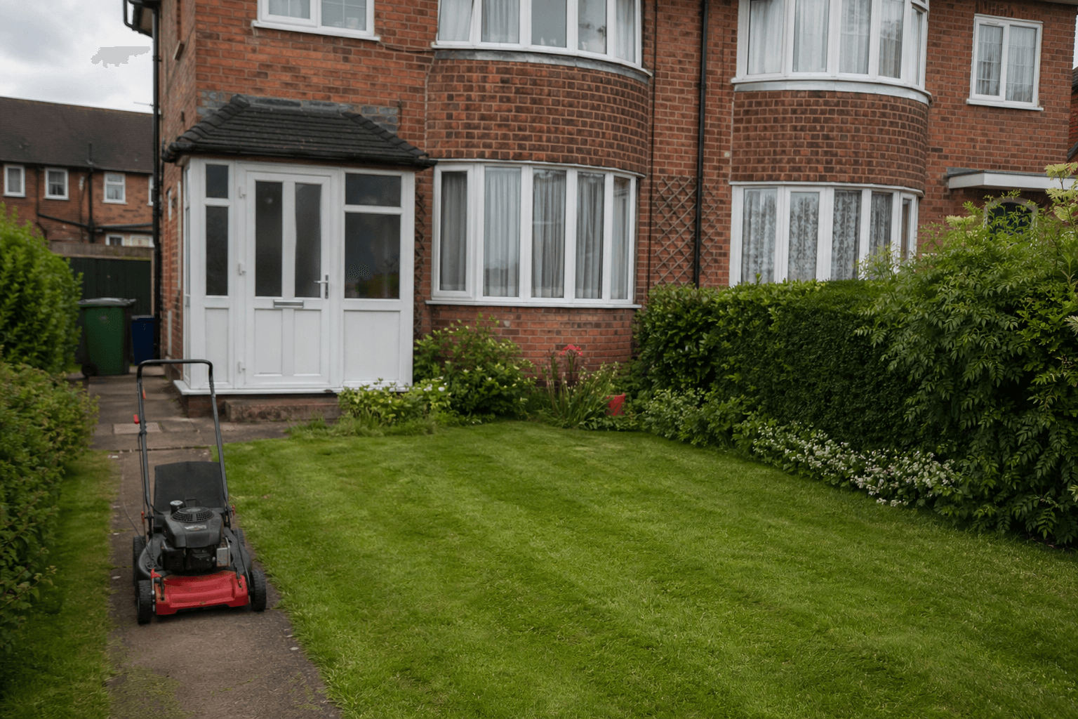 UK suburban front garden with petrol mower on path after mowing [dedupe:taskino:blog:starting-lawn-care-bare-minimum-uk:hero]