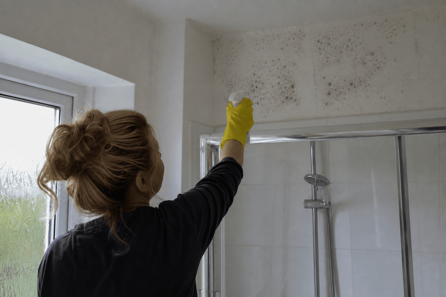 UK homeowner treating black mould on a bathroom wall with fungicidal spray