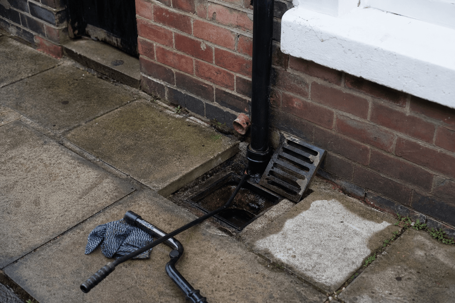 Outside drain gully and drain rods on paving at a UK terraced house