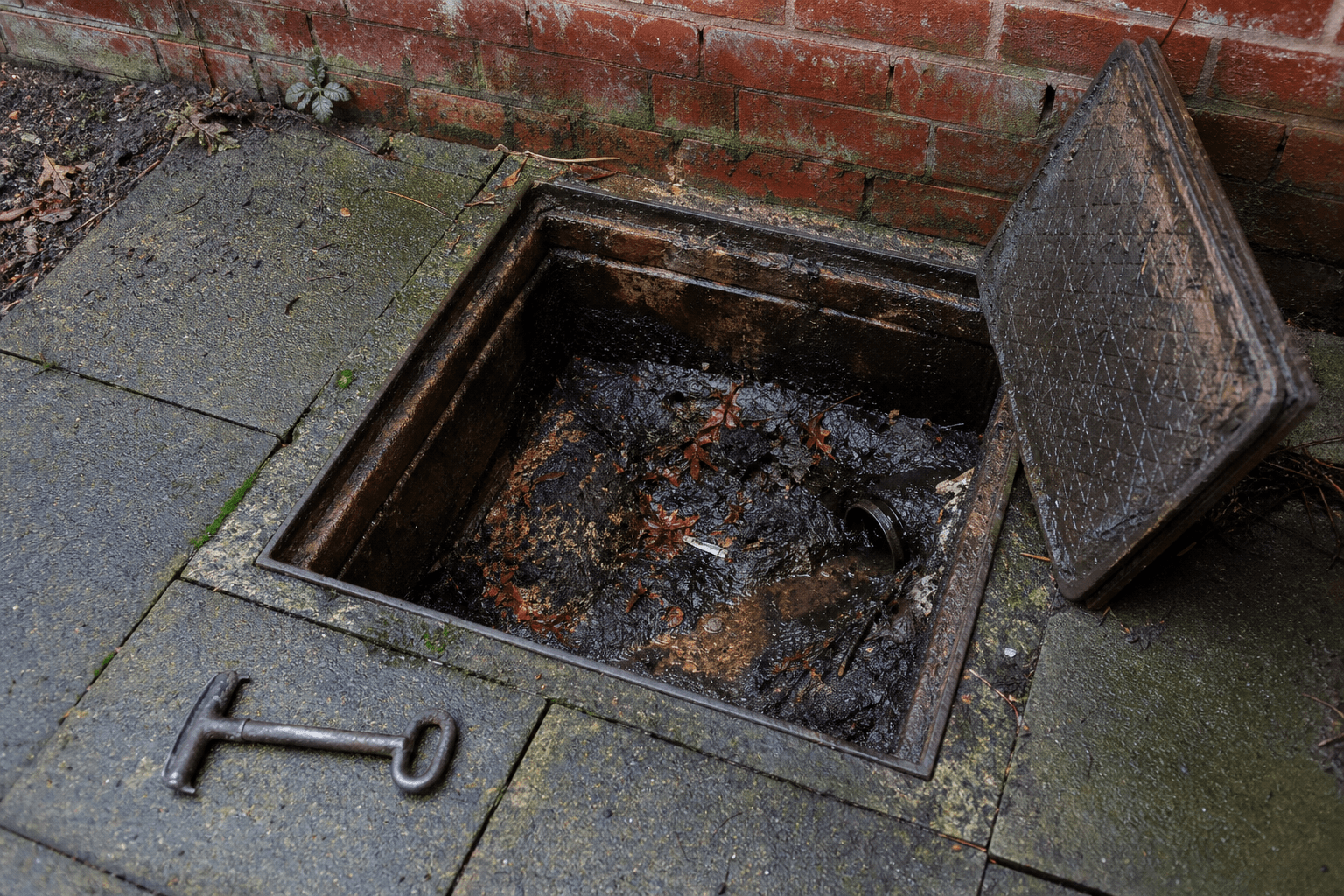 Open UK inspection chamber with leaves, silt and grease in a back garden