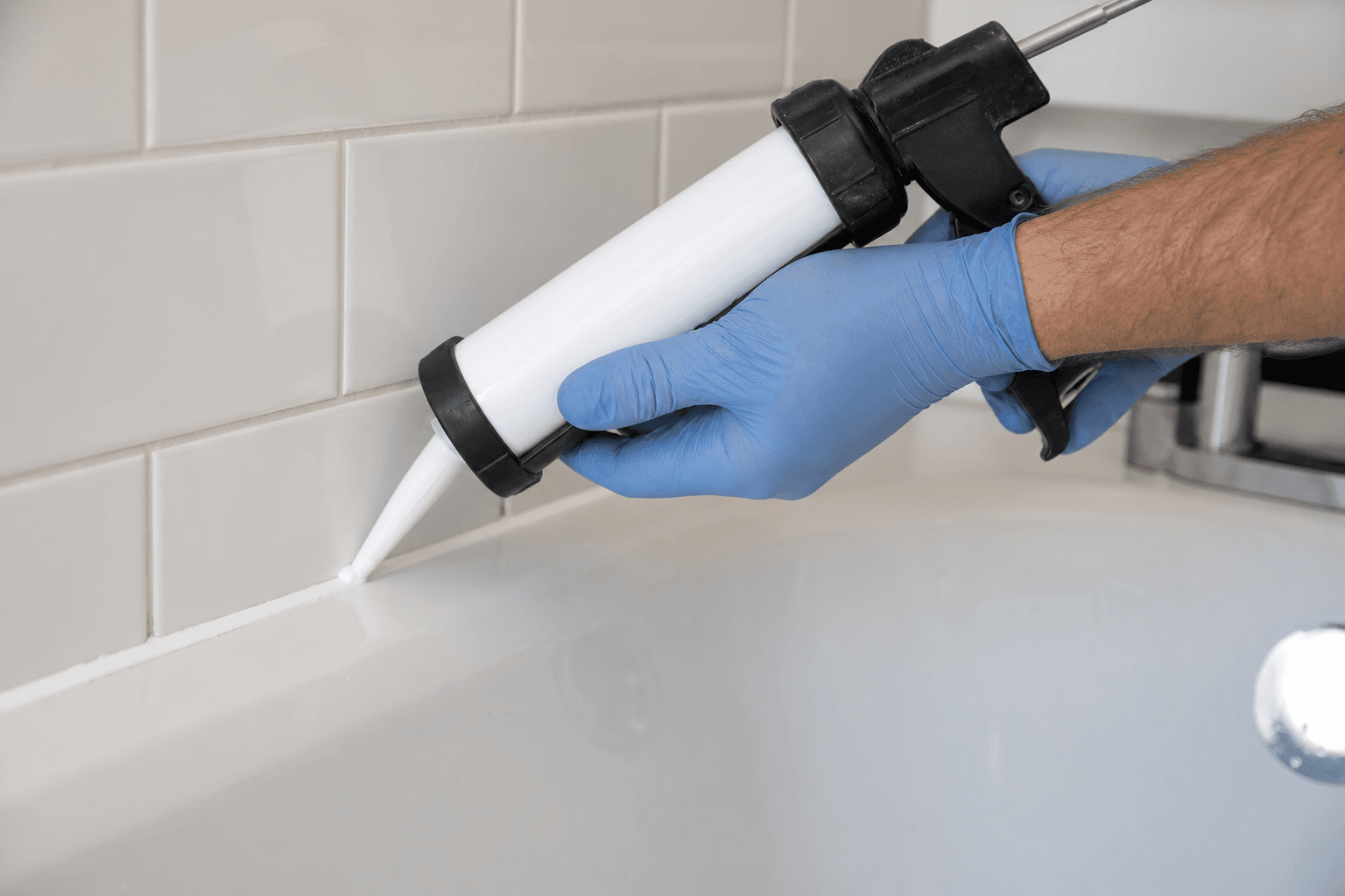 Hand applying anti-mould silicone sealant along a bath-tile joint in a UK bathroom