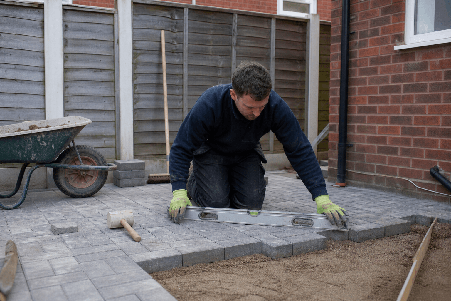 Homeowner DIY laying block paving on a small UK patio with spirit level and rubber mallet