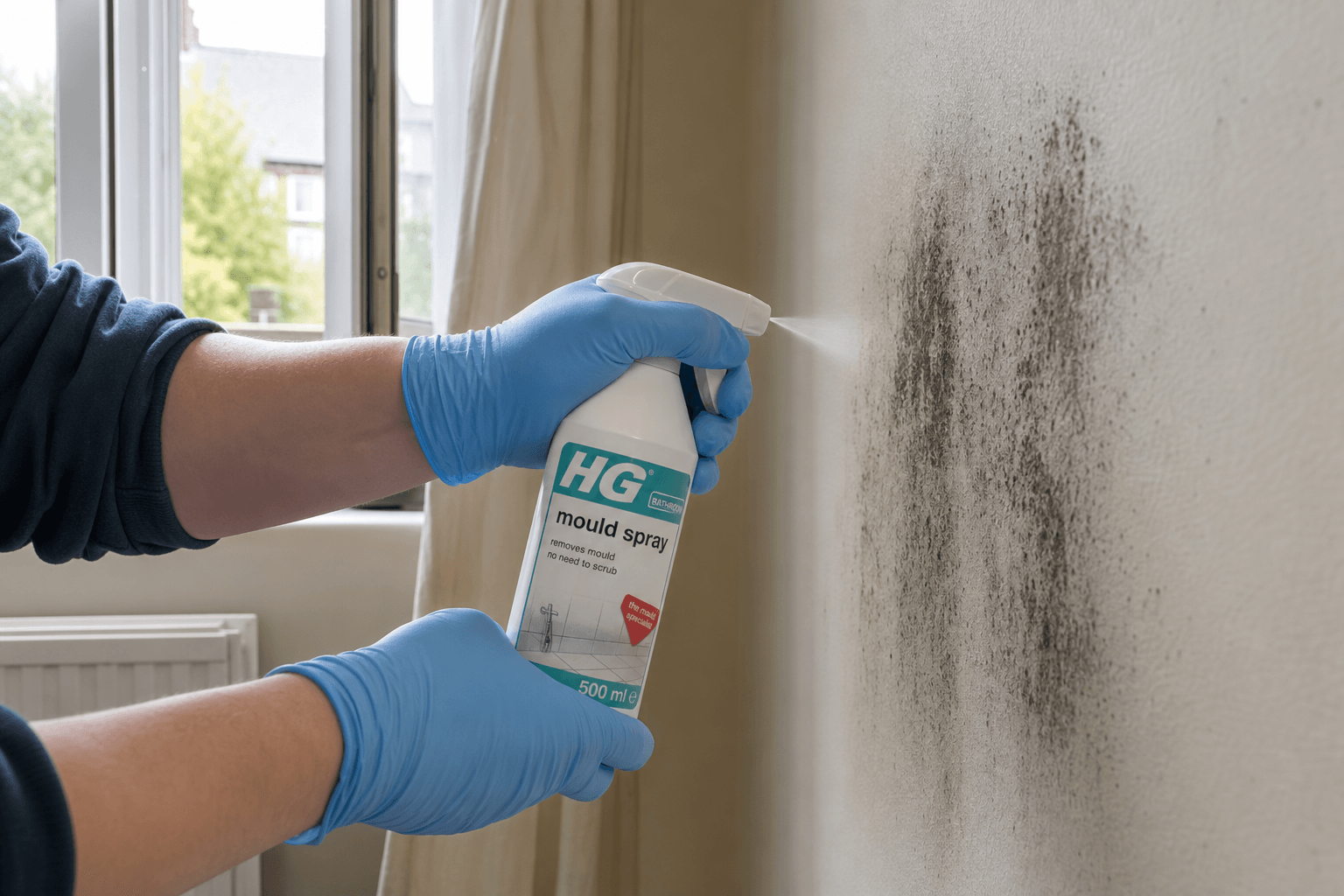 Gloved hands spraying mould biocide on wall patch in UK home
