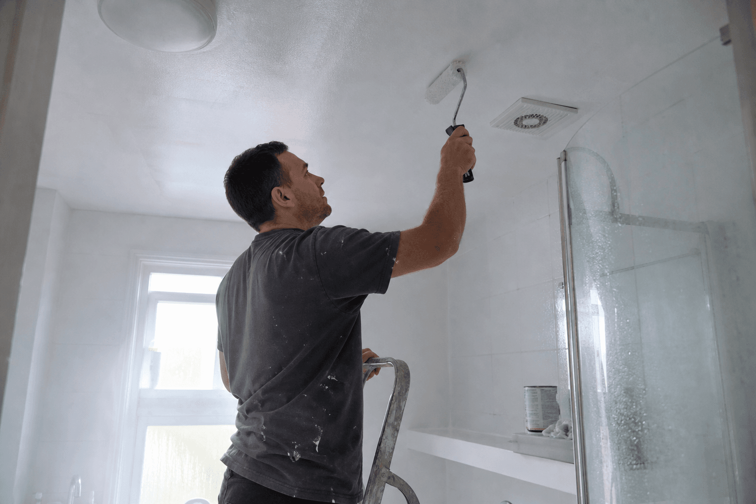 Homeowner painting a UK bathroom ceiling with anti-mould paint