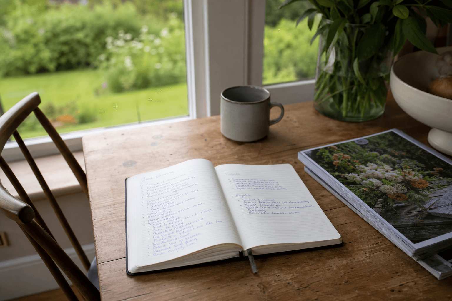 Open notebook on a UK kitchen table by a window overlooking the garden, planning gardener hire