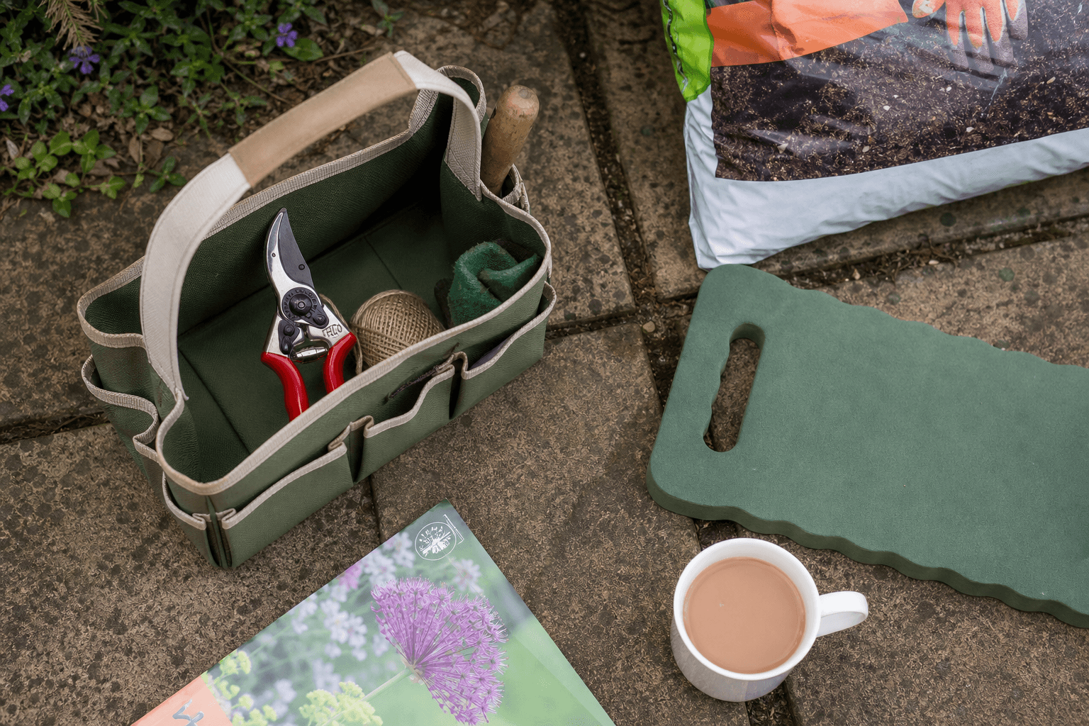 Top-down flat-lay of UK garden tools on a stone patio with secateurs, kneeling pad and compost