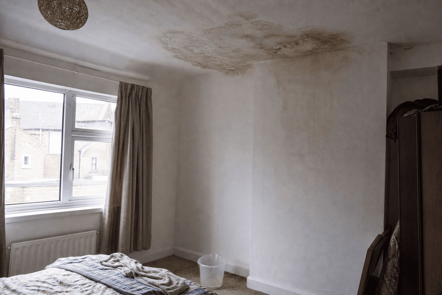 Damp patch on a UK bedroom ceiling near a chimney breast with a bucket on the floor